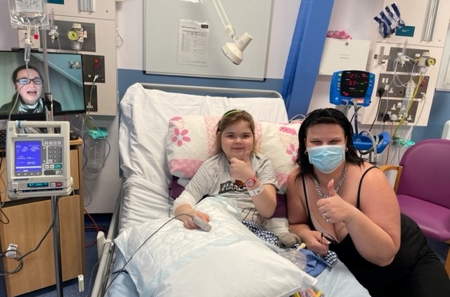 Child in bed, next to mother both with thumbs up