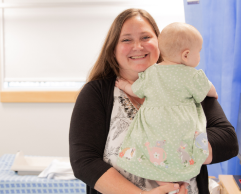 A mother with long straight hair holding her young baby in her arms. mum is smiling