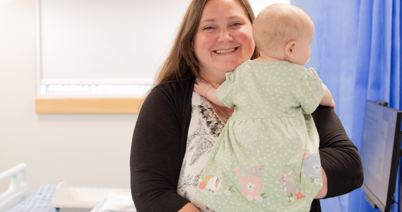 A mother with long straight hair holding her young baby in her arms. mum is smiling