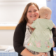 A mother with long straight hair holding her young baby in her arms. mum is smiling